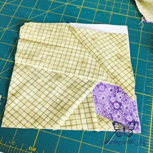 Foundation paper pieced block with purple butterfly wing in bottom right corner and green grid fabric outlining it.