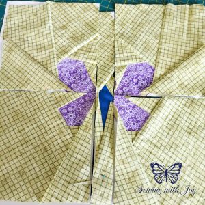Four square foundation paper pieced blocks and one rectangular block in the middle, form a purple and blue butterfly on green background.