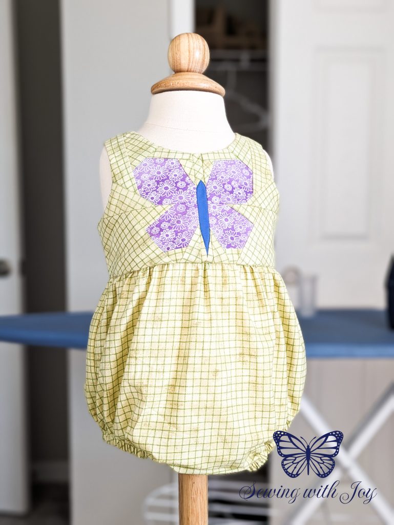 Completed green romper with paper pieced butterfly on the bodice. The romper has no sleeves is on a child sized dress form.